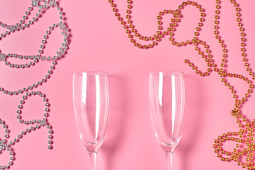 Two empty glass for alcohol near necklaces golden and silver colors lies on pink table. Top view. Close-up