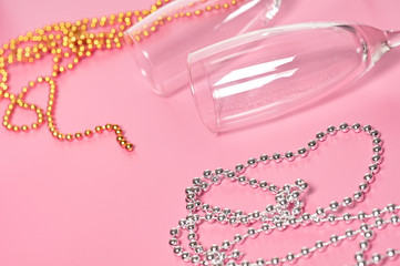Two empty glass for alcohol near necklaces golden and silver colors lies on pink table. Close-up
