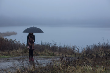 young girl with black umbrella on background dark foogy lake