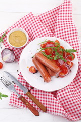Fried sausages with tomatoes, onions, arugula and mustard on a white wooden background