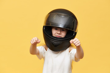Transportation, extreme, motorsports and activity concept. Portrait of dangerous little girl rider in black protective motorcycle helmet keeping hands in front of her as if driving motorbike