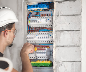 Man, an electrical technician working in a switchboard with fuses. Installation and connection of electrical equipment.