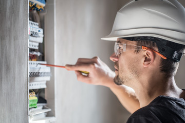 man, an electrical technician working in a switchboard with fuses. Installation and connection of electrical equipment. Close up. - obrazy, fototapety, plakaty