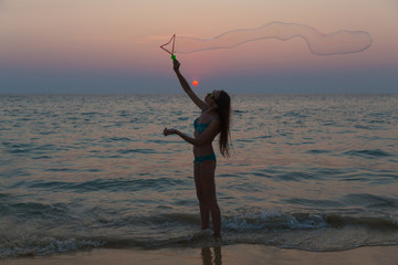 Fototapeta premium Young attractive girl blowing bubbles on the beach at sunset