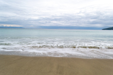 Fototapeta na wymiar Long calm waves at sea shore over cloudy sky
