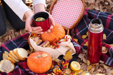 Children's hands hold a red mug with tea in the autumn park