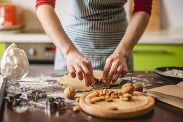 Cook housewife making Christmas cookies at home on a colorful kitchen. Hands making dough the shape of Christmas trees