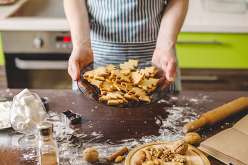 Cook housewife making cookies at home on a kitchen. Woman holding freshly baked cookies in the shape of Christmas trees