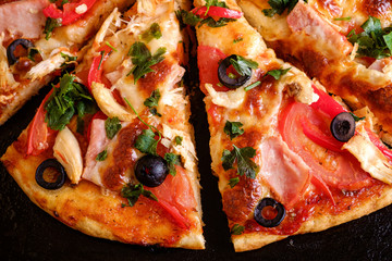 Fresh hot homemade pizza with chicken meat, ham, tomato, mozzarella cheese, black olives and parsley, top view