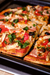Fresh hot homemade pizza with chicken meat, ham, tomato, mozzarella cheese, black olives and parsley, angle view