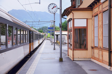 Passenger train departs from the railway station platform in Swiss Alps.