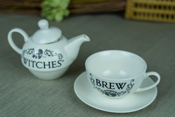 Witch tea party, white teapot and cup on gray linen  tablecloth