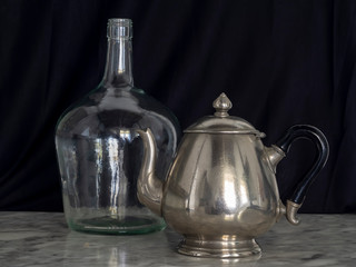 Silver Teapot and Demijohn Black Background Marble Table