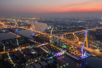 Evening bridge with lights on the bridge over the Chao Phraya River. Aerial view of the Bhumibol Adulyadej Suspension Bridge over the Chao Phraya River in Bangkok with cars on the bridge at the sunset