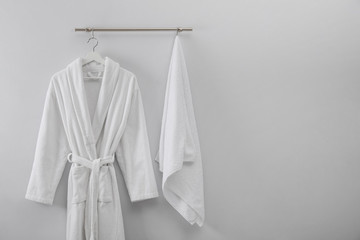 Hanger with clean bathrobe and towel on light wall. Space for text - obrazy, fototapety, plakaty