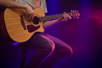 Plakat The musician plays an acoustic guitar. Beautiful background with colored light rays.