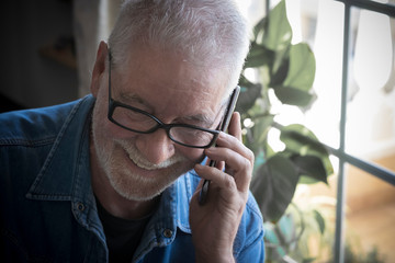 Attractive senior people with white beard and eyeglasses using the cellphone. Smiling listening good news. One caucasian man