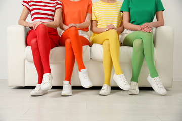 Fototapeta na wymiar Women wearing bright tights sitting on sofa indoors, closeup