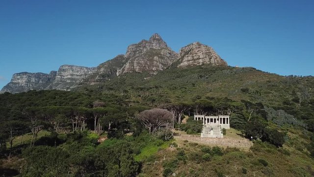 4K aerial summer sunny morning footage of beautiful green Devil's Peak slopes with white stone columns Cecil Rhodes Monument, Table Mountain National Park, Cape Town, Western Cape, South Africa