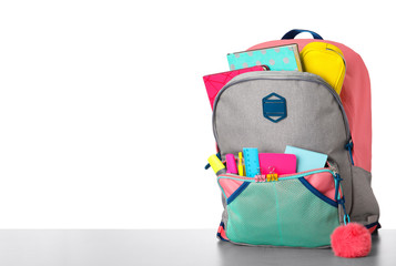 Bright backpack with school stationery on grey stone table against white background