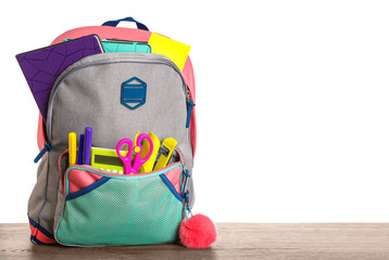 Bright backpack with school stationery on wooden table against white background