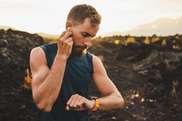 Male runner synchronizing wireless earphones with smart watch. Preparing for trail running outdoors...