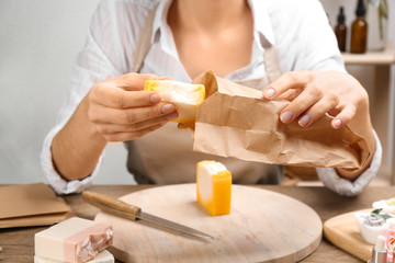 Obraz na płótnie Canvas Woman putting natural handmade soap into paper bag at wooden table, closeup