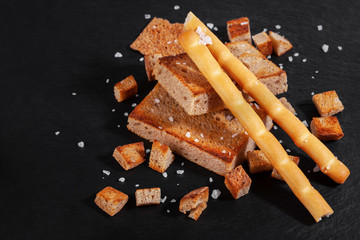 Rye crackers and salty sticks, stacked on a slide, on a dark board.