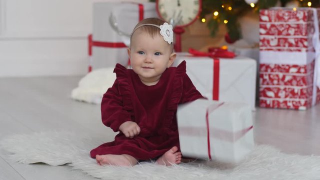 Little baby girl sit on parquette floor play with christmas present box at home