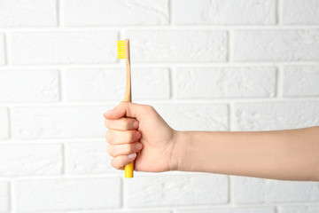 Woman holding bamboo toothbrush against white brick wall, closeup