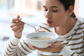 Young woman eating tasty vegetable soup indoors