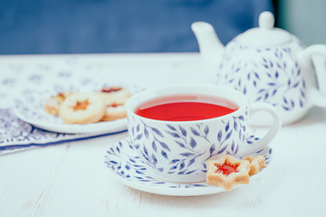 Pink fruit tea and homemade cookies stars with jam on a white wooden background
