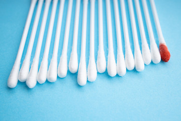 Blood on the hygiene cotton stick. Menstruation. Skincare mockup for design. Stack of disposable cotton stick on a blue background. Cosmetology concept. Bloody wound. Injury.