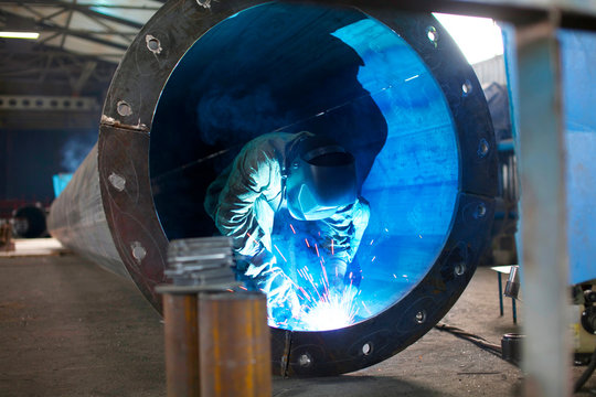 Portrait of a factory welder working at the plant. Metallurgical plant for the production of metal structures. Worker in a welding mask protected from dropping sparks.