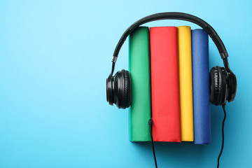 Books and modern headphones on light blue background, top view. Space for text