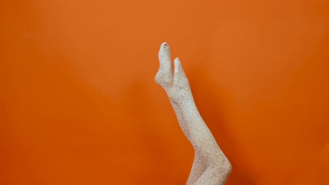 White fishnet stockings on perfect woman legs over bright orange background in studio