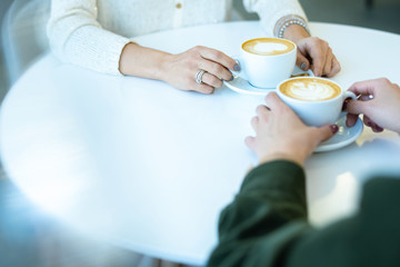 Hands of two young friendly women having cappuccino by table in cafe