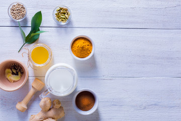 Ingredients for Golden Latte on a white wooden background. Ginger root, milk, turmeric, cardamom, allspice peas.