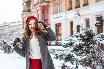 Happy smiling girl enjoying winter holidays, walking in snow covered street of European city. Model...