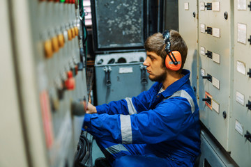 Marine engineer inspecting ship's engine or generators in engine control room ECR. Seamen's work.