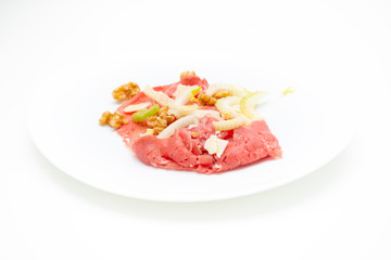 albese meat with savoy cabbage, walnuts, celery and parmesan cheese in the foreground on plate and white background
