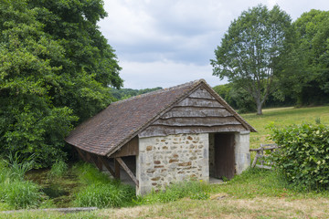 France. Sarthe. Lavoir traditionnel en pierre et toit de tuiles. Traditional stone wash-house and tiled roof.
