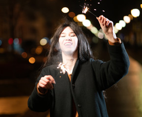 beautiful girl with sparklers in the evening on the street. festive mood sparkling hand-held...