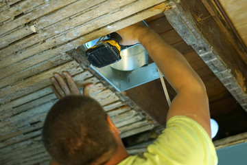Workman fixing the exhaust fan on the wall.