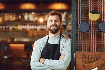Bearded smiling barman waiter standing on the background of a bar.