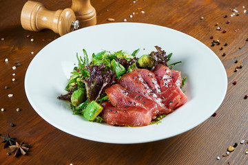 Fresh and delicious Tataki salad with tuna, lettuce, avocado. Tasty seafood salad of Japanese cuisine in white bowl on wooden background. Close up food photo