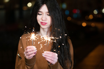 beautiful girl with sparklers in the evening on the street. festive mood sparkling hand-held fireworks.