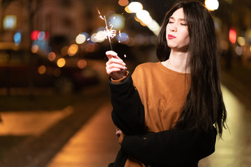 beautiful girl with sparklers in the evening on the street. festive mood sparkling hand-held...