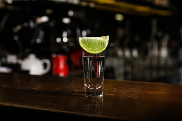 Mexican Tequila shot with lime slice on wooden bar counter