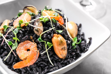 Delicious black risotto with seafood in bowl on table, closeup